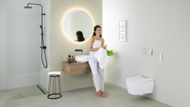 Женщина опирается на раковину в ванной комнате с унитазом-биде Geberit AquaClean Sela, а также раковиной и мебелью Geberit VariForm