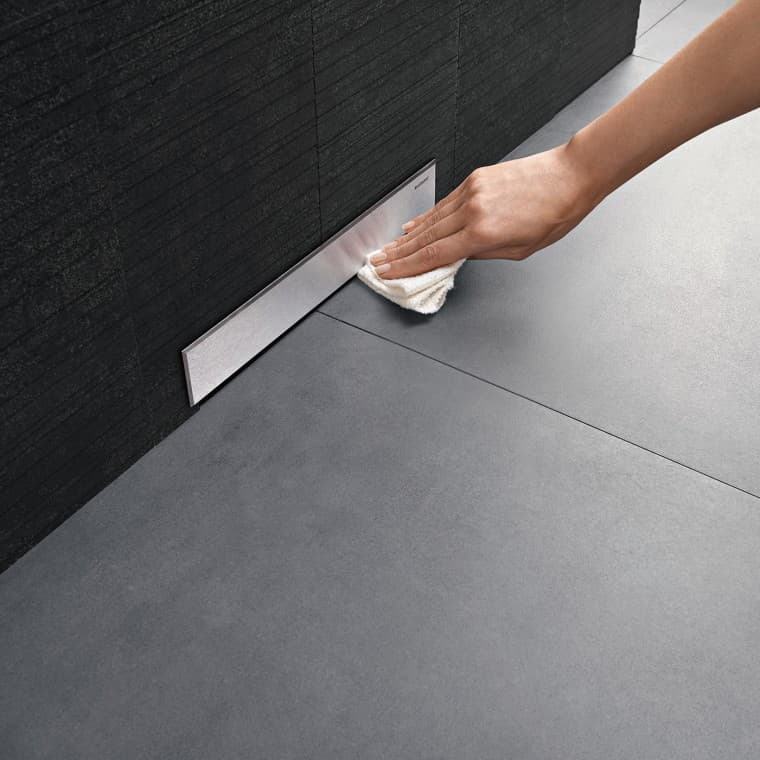 Рука очищает декоративную накладку трапа Geberit, монтируемого в стену Рука очищает декоративную накладку трапа Geberit, монтируемого в стену